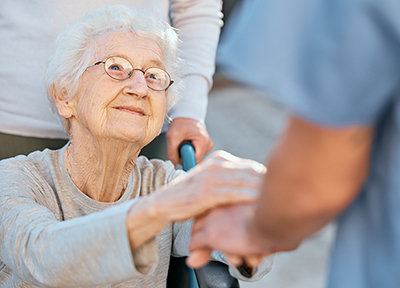 Holding hands, caregiver and senior woman in wheelchair for support outdoor in retirement home. Love, trust and healthcare nurse or medical wellness doctor for disability patient with kindness.